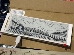 Acrylic e-paper display with countryside landscape design, used for DIY electronics projects.