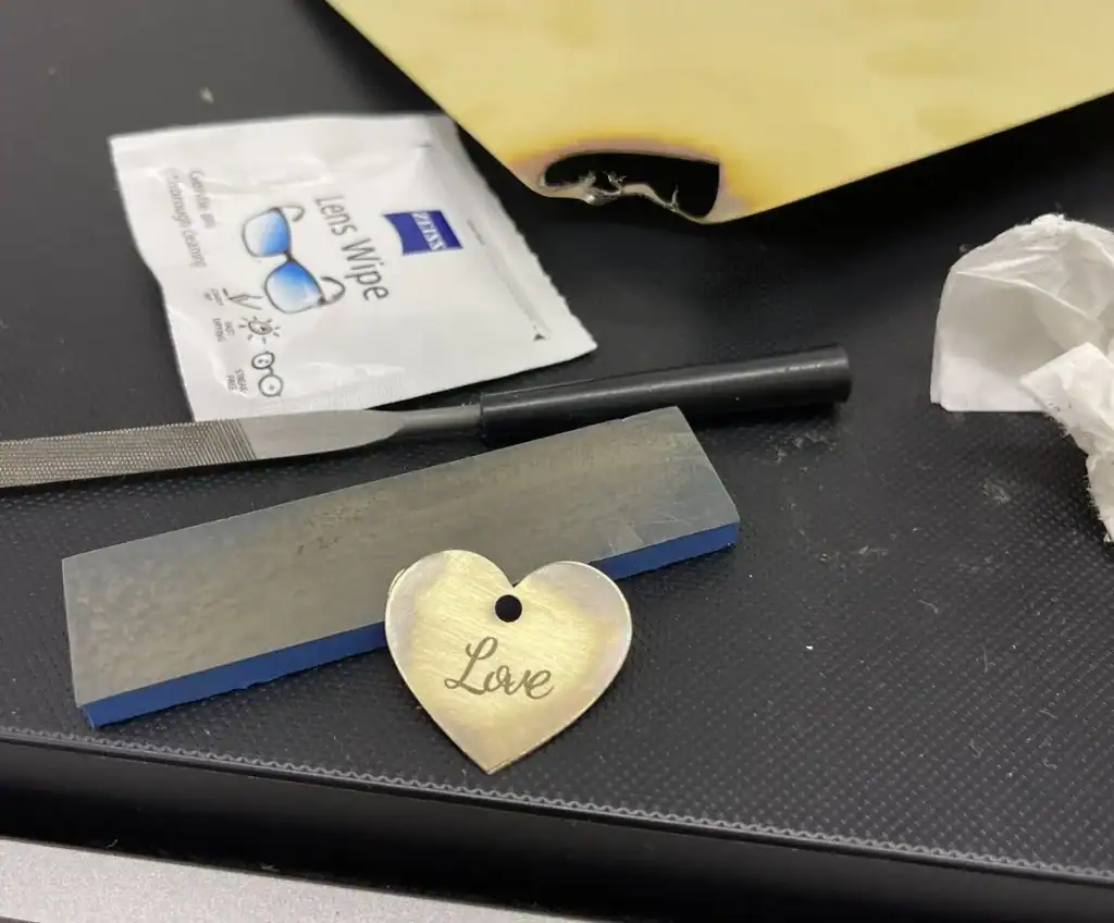 Polishing heart-shaped pendant with "Love" inscription on a black work surface.