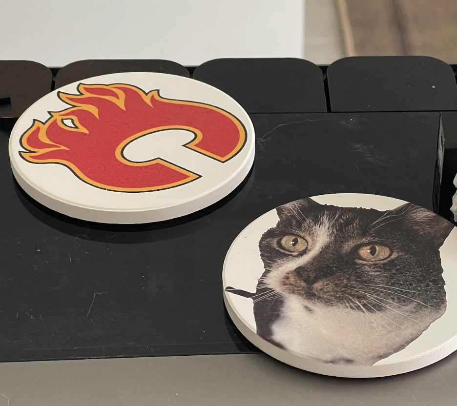 Custom printed round coasters featuring a Penny the cat's face and Calgary Flames logo