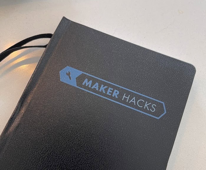 Maker Hacks notebook with blue logo on black cover for DIY projects and hacking ideas.