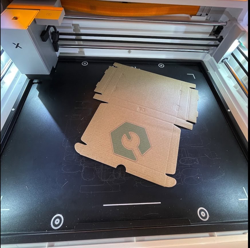 Cardboard pieces on xTool M2 laser cutter bed for printing or engraving.