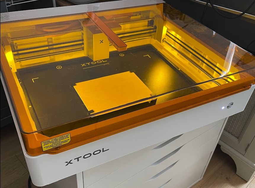 XTool M2 laser cutter with yellow protective cover and workspace.
