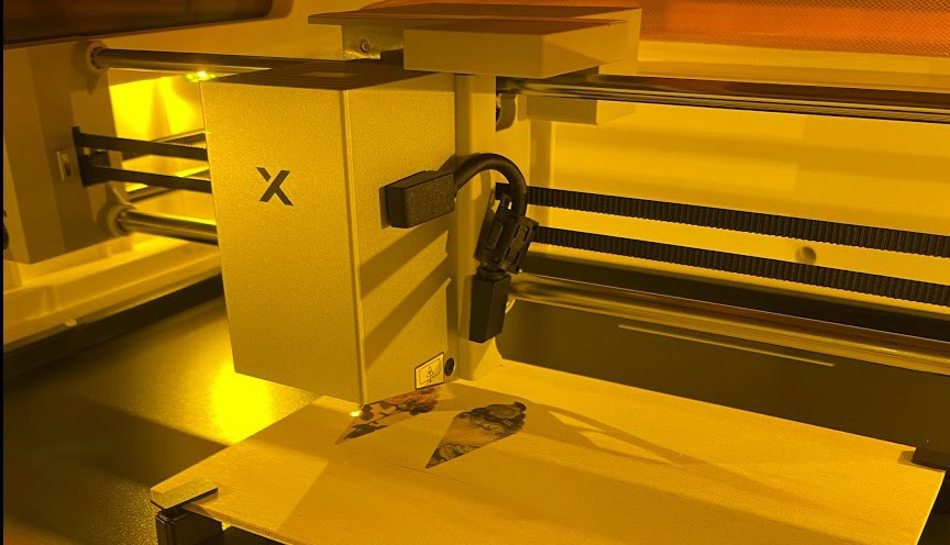 XTool M2 laser engraver and cutter in operation on a wooden surface.